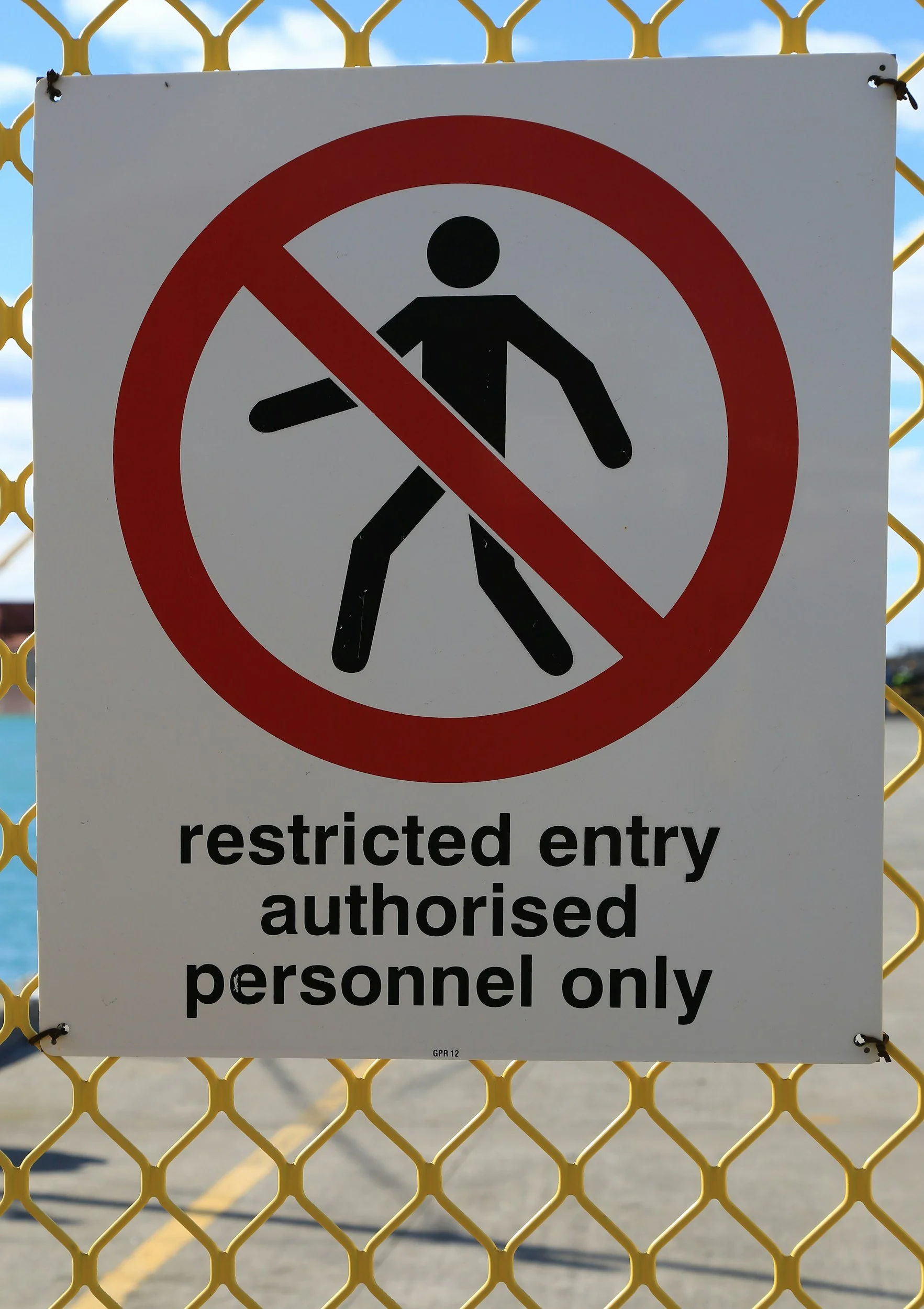 A sign on a yellow chain-link fence indicating restricted entry, with a black silhouette of a walking person inside a red circle with a line through it, and text that reads 'restricted entry authorized personnel only'.