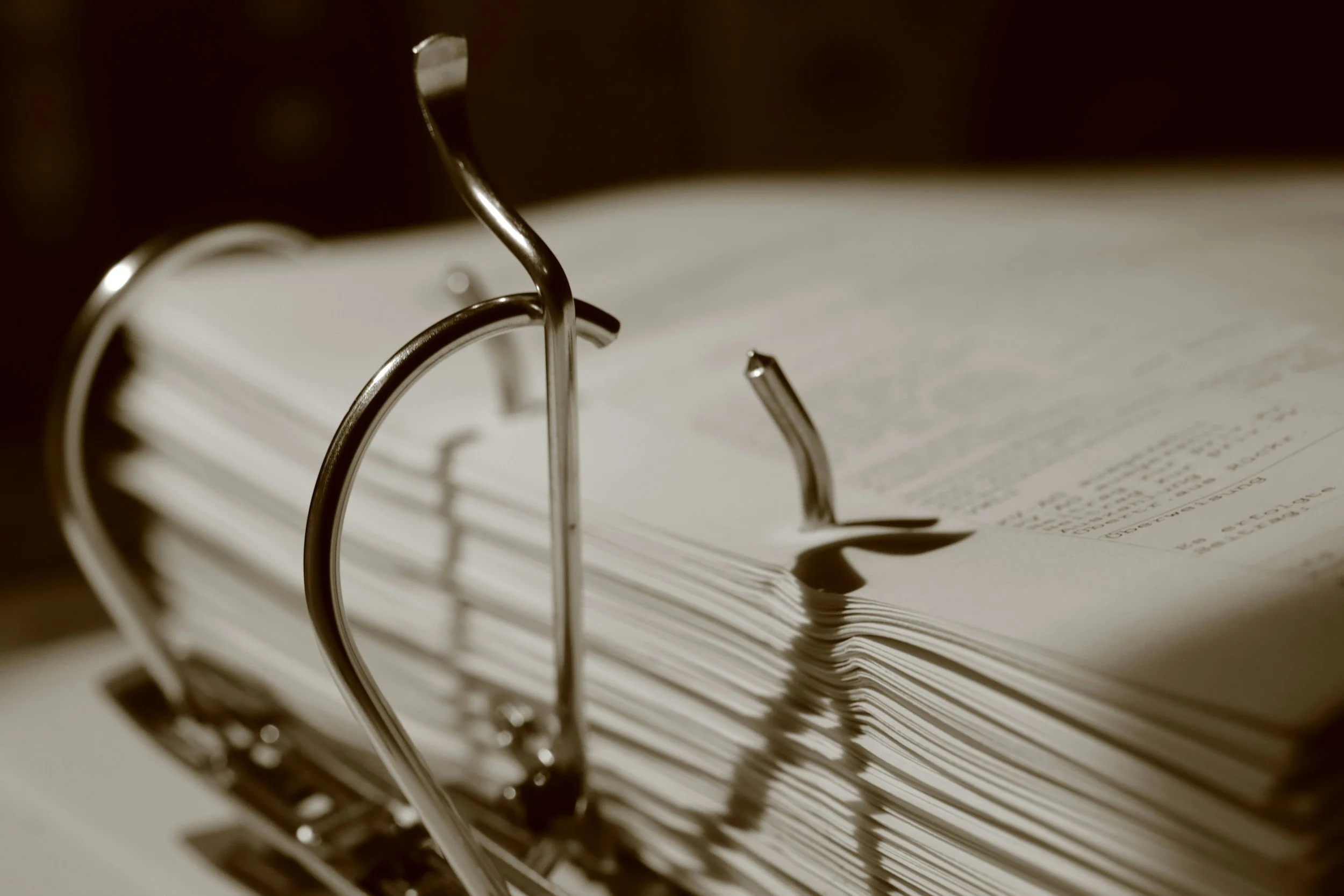 Close-up of a thick, spiral-bound notebook with pages slightly curled and shadows cast by the metal rings.