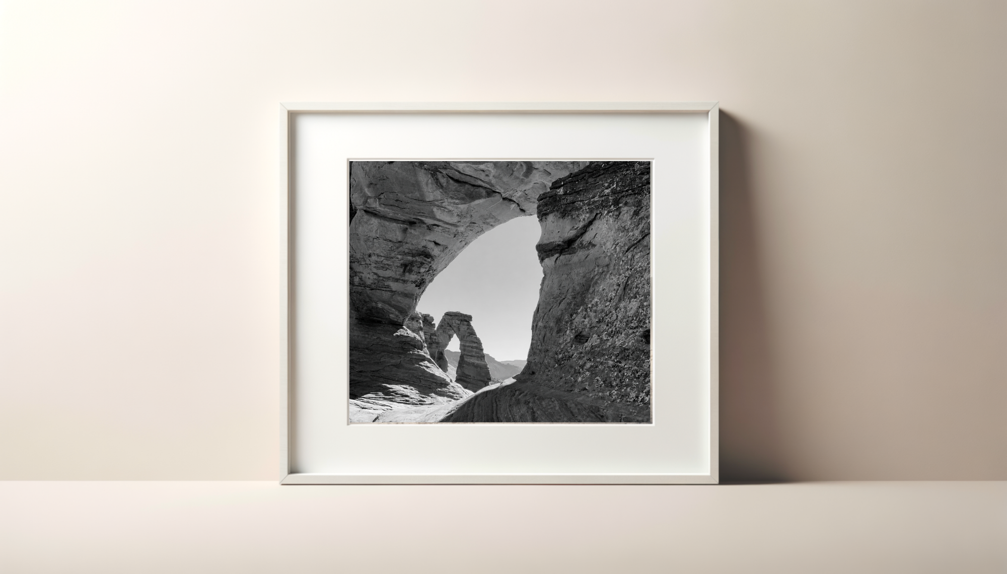 Black and white photograph of a rock formation with arches and layered textures, framed and hanging on a plain white wall.