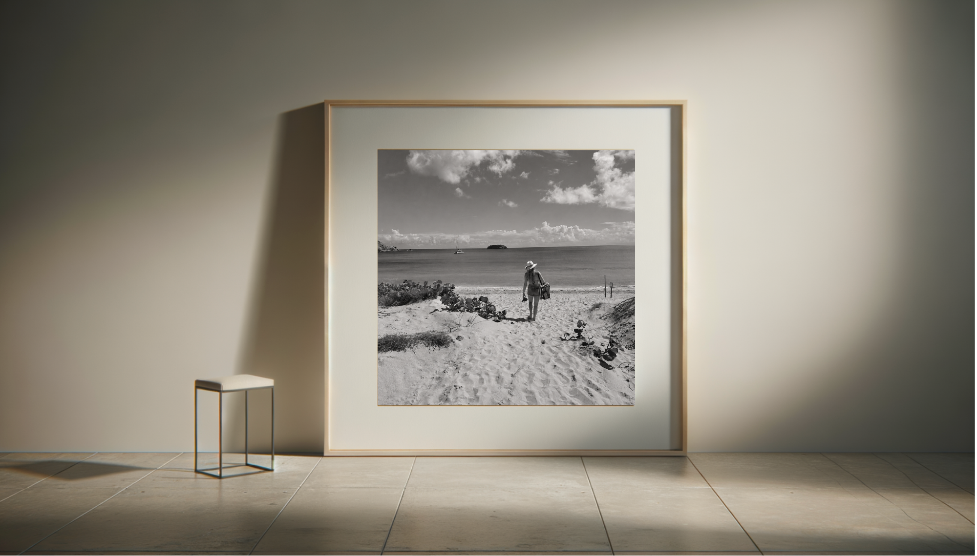 Black and white photograph of a woman walking on a sandy beach, carrying a bag and wearing a hat, with ocean and clouds in the background.