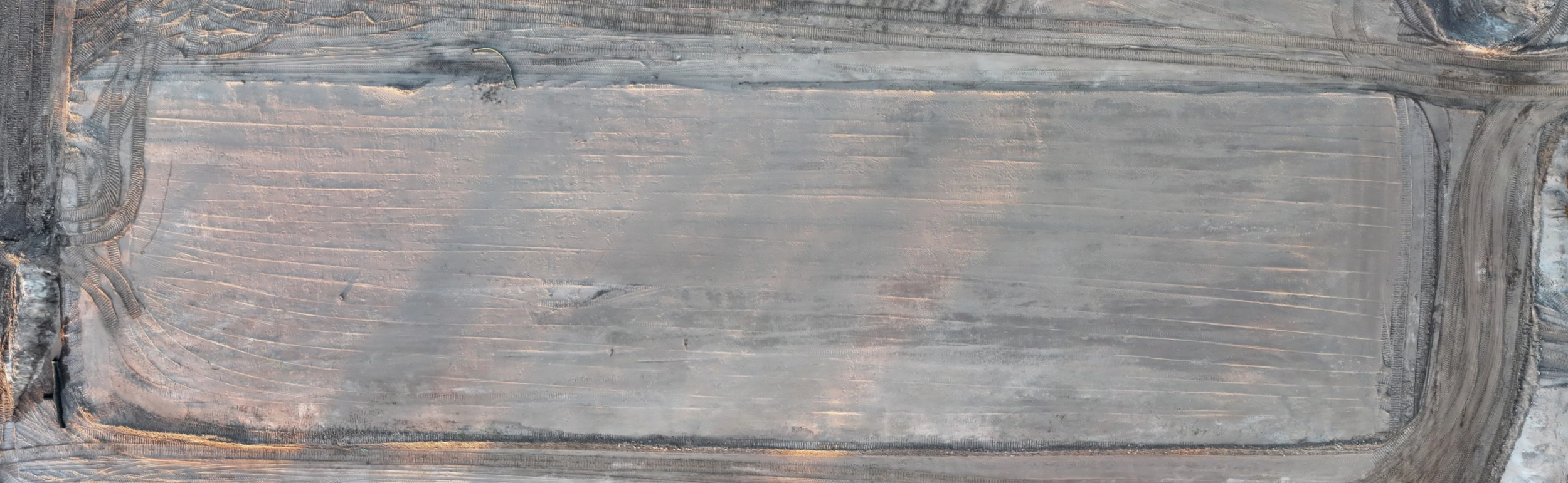 Aerial drone view of earthwork and grading progress on a construction site showing a leveled and compacted building pad with visible grading marks and perimeter access roads.