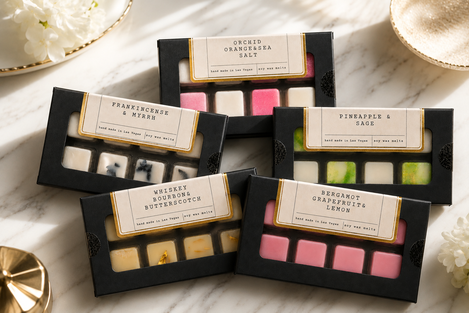 Four boxes of soy wax melts with various scents, arranged on a marble surface, surrounded by decorative flowers and dishes.