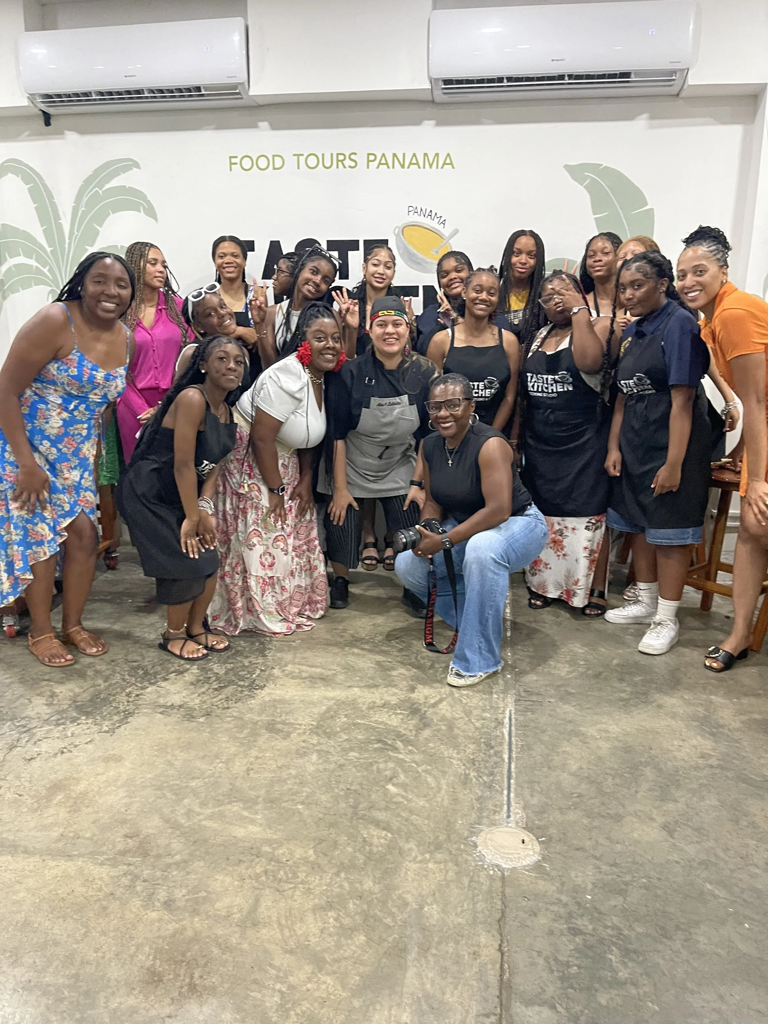 A group of women and girls standing and sitting together in front of a wall with the words 'Food Tours Panama' and a logo. Some are smiling and making peace signs. They appear to be in a casual indoor setting.