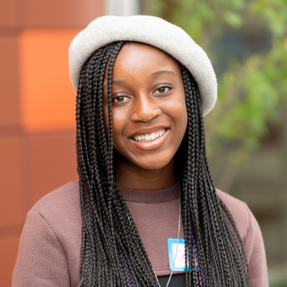 Young woman with braided hair wearing a white beret, smiling outdoors.