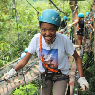 Young woman smiling while zip-lining through a forest, wearing a blue helmet and harness.