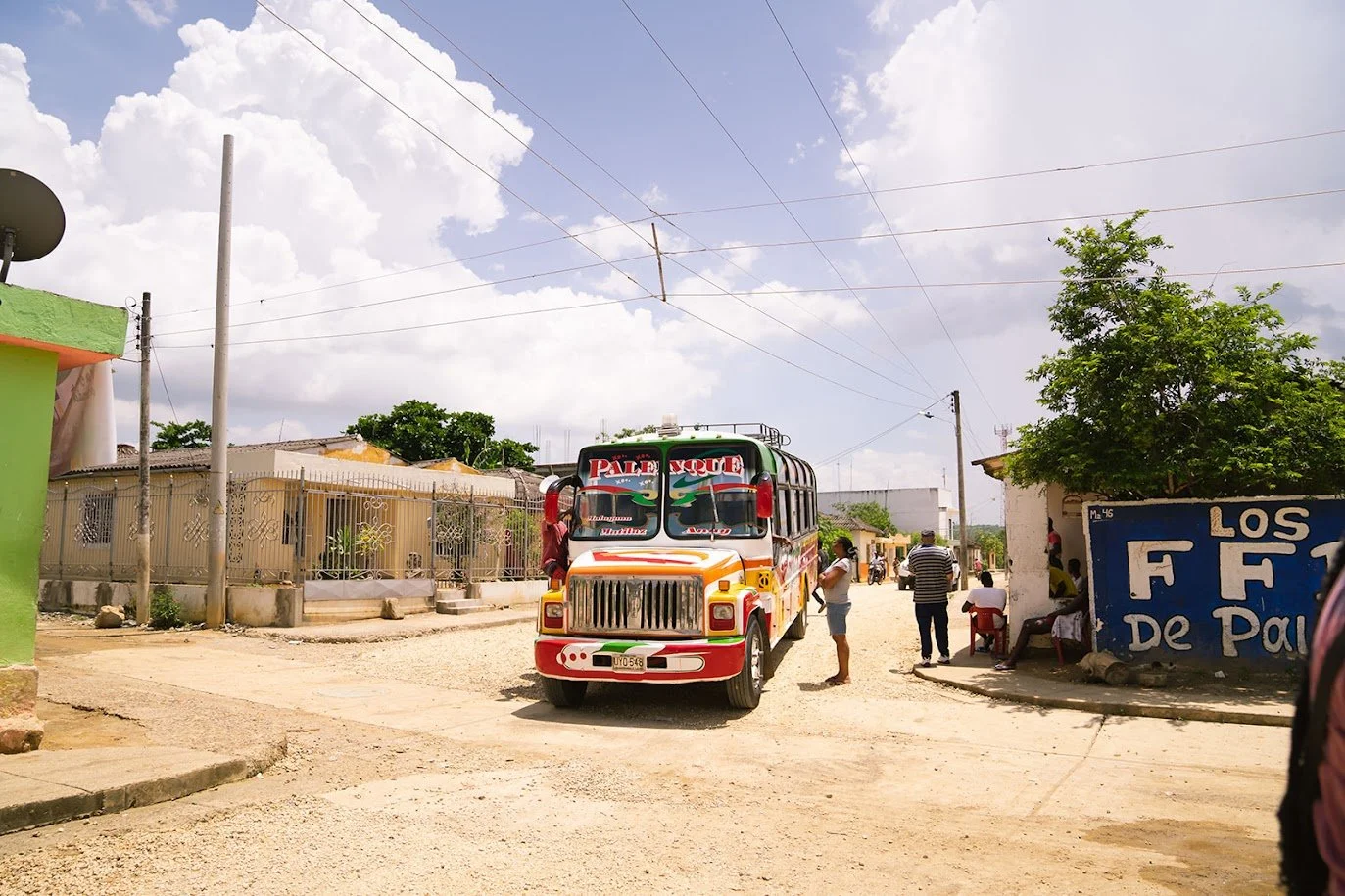 Street scene with a colorful bus, people, and buildings in a small town under a partly cloudy sky.