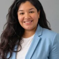 A woman with long, dark hair wearing a light blue blazer smiling at the camera.