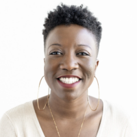Close-up of a smiling Black woman with short curly hair, wearing a cream-colored top and large hoop earrings, against a white background.