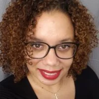 Close-up photo of a woman with curly hair, glasses, and red lipstick, smiling at the camera.