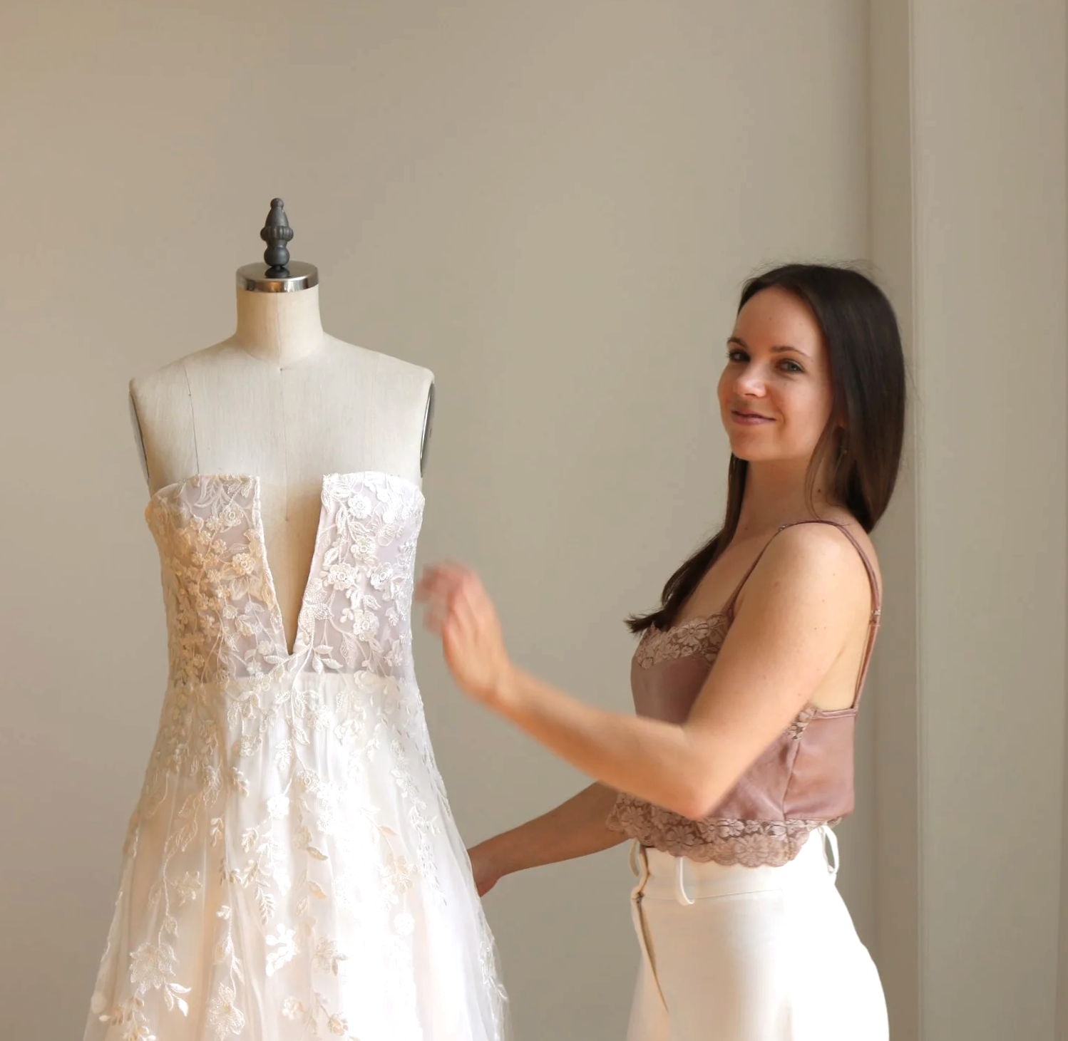 Frau präsentiert ein weißes Brautkleid mit Spitzenapplikationen an einem Schneiderpuppen.
