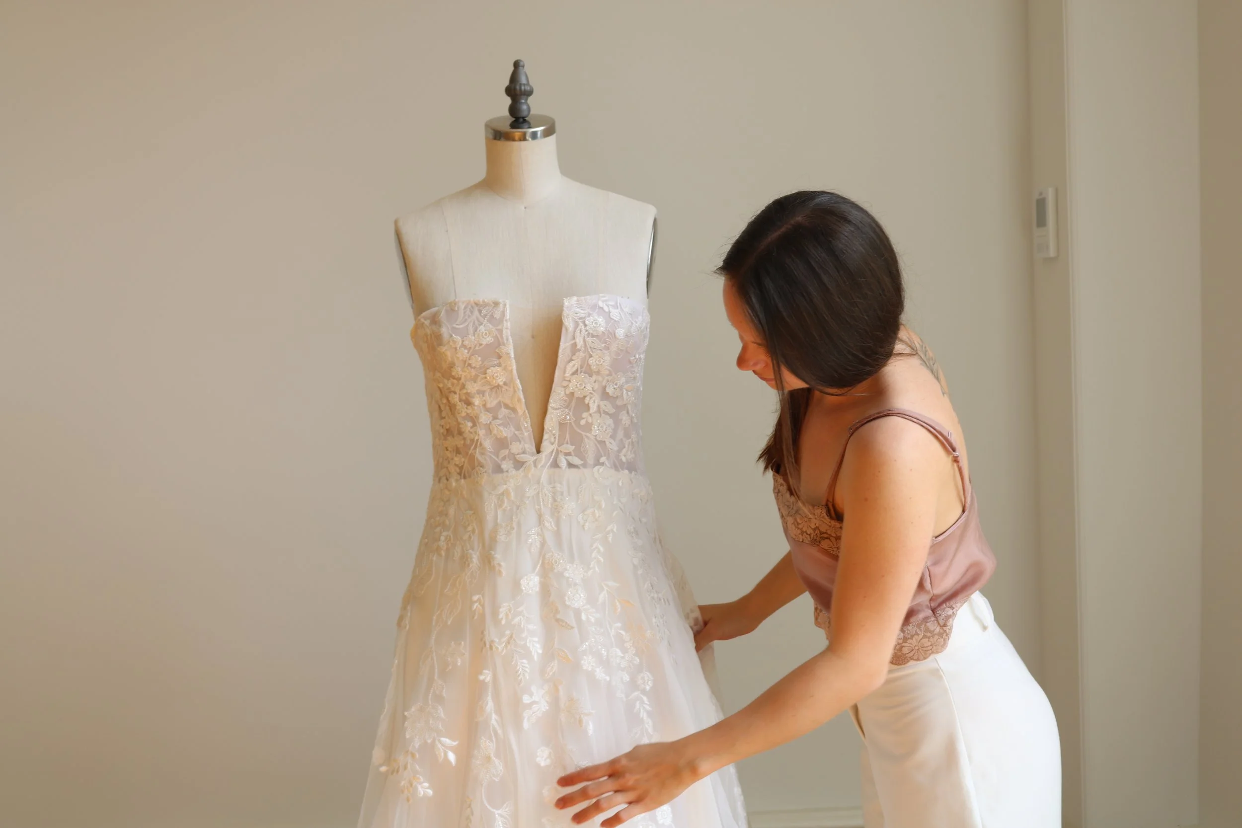 Eine Frau passt ein Brautkleid an einer Schneiderpuppe an.