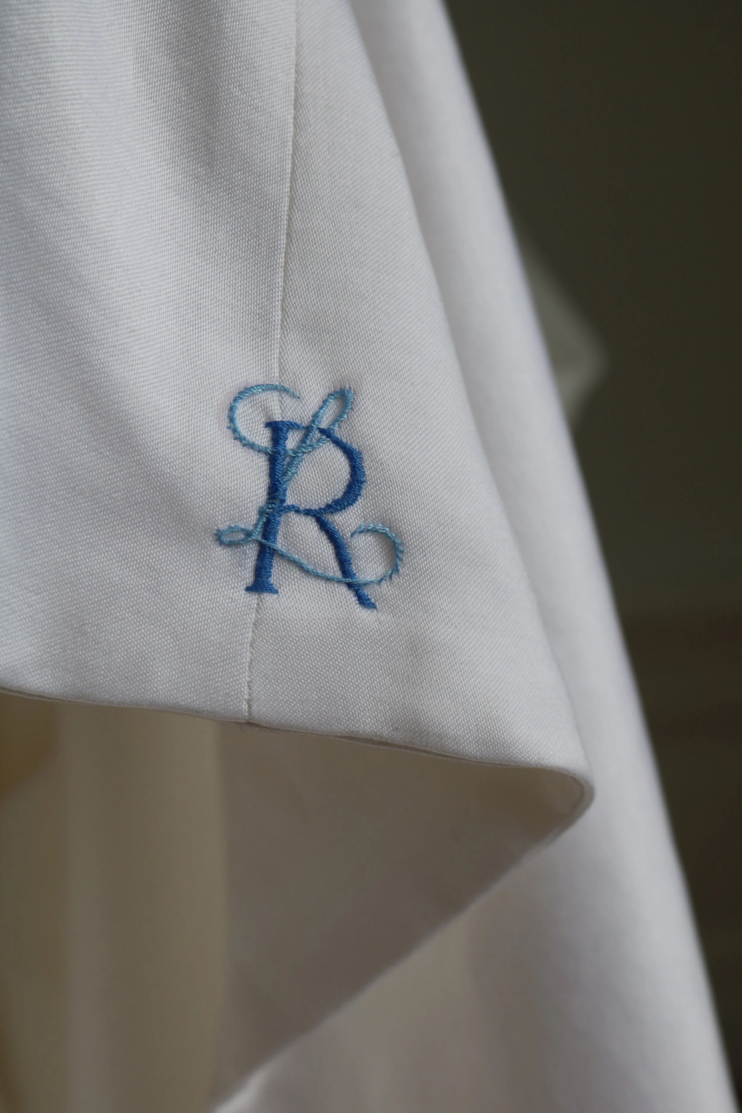 Nahaufnahme eines weißen Stoffkleides mit einer blauen Stickerei in Form eines Monogramms.