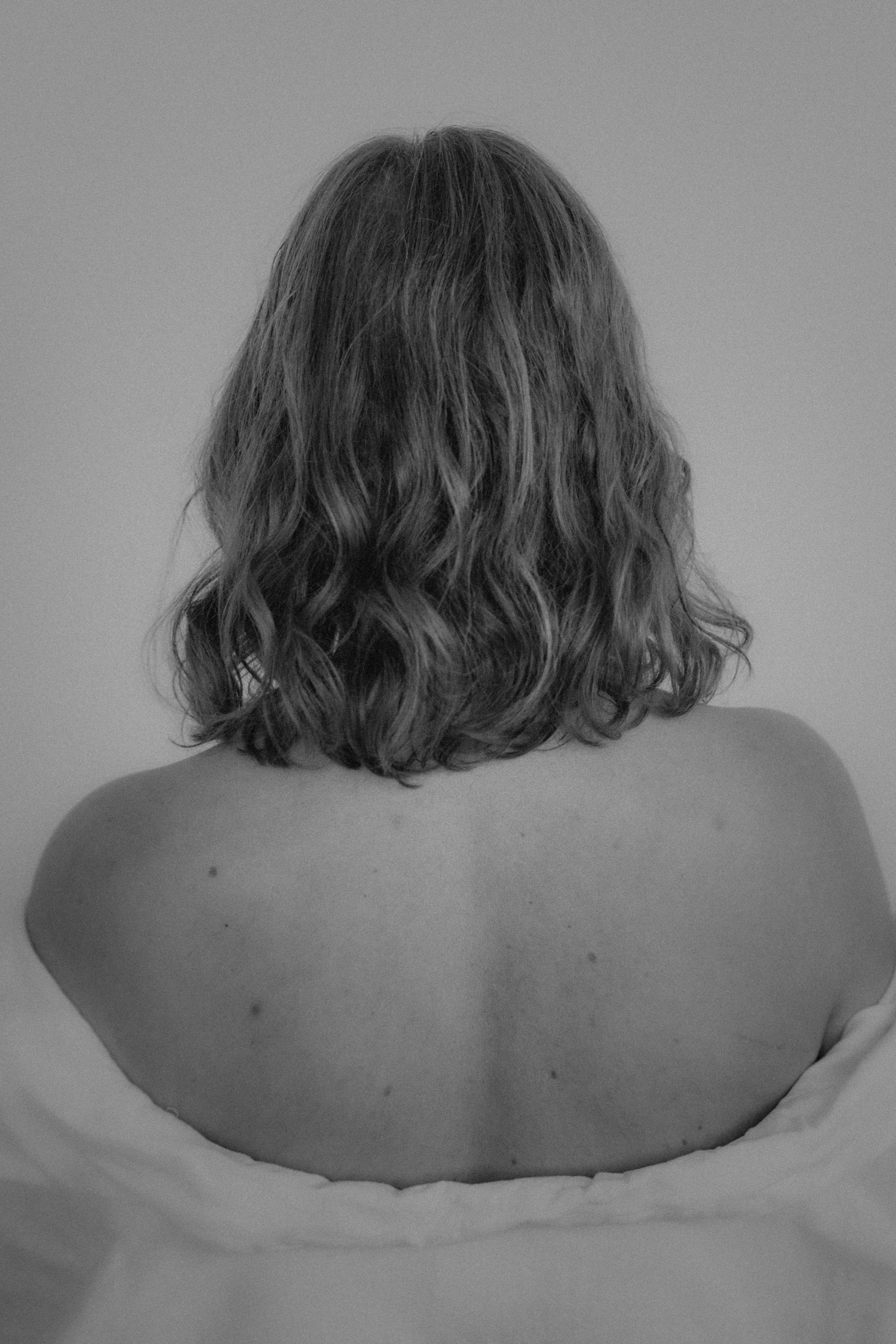 Back view of a person with shoulder-length wavy hair, sitting in a roll of toilet paper or paper towel.