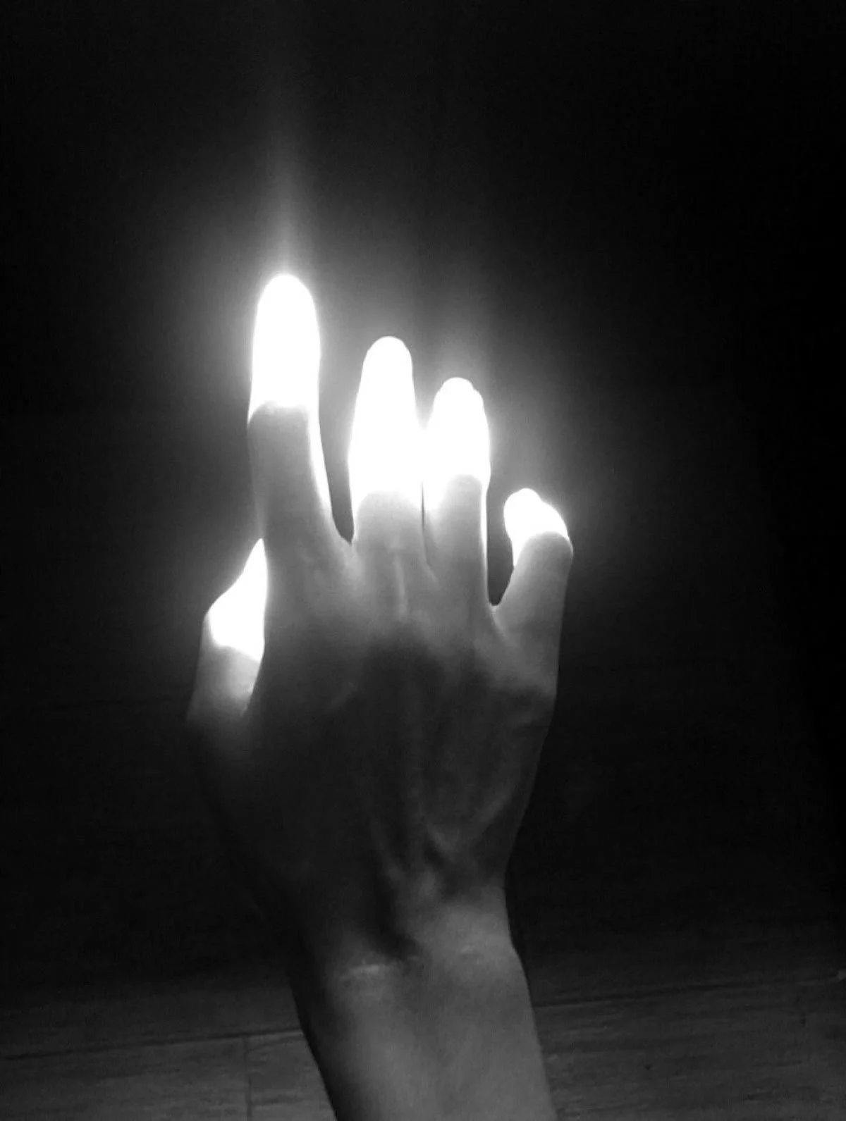 Black and white photo of a hand reaching towards a bright source of light, with fingers slightly spread apart.