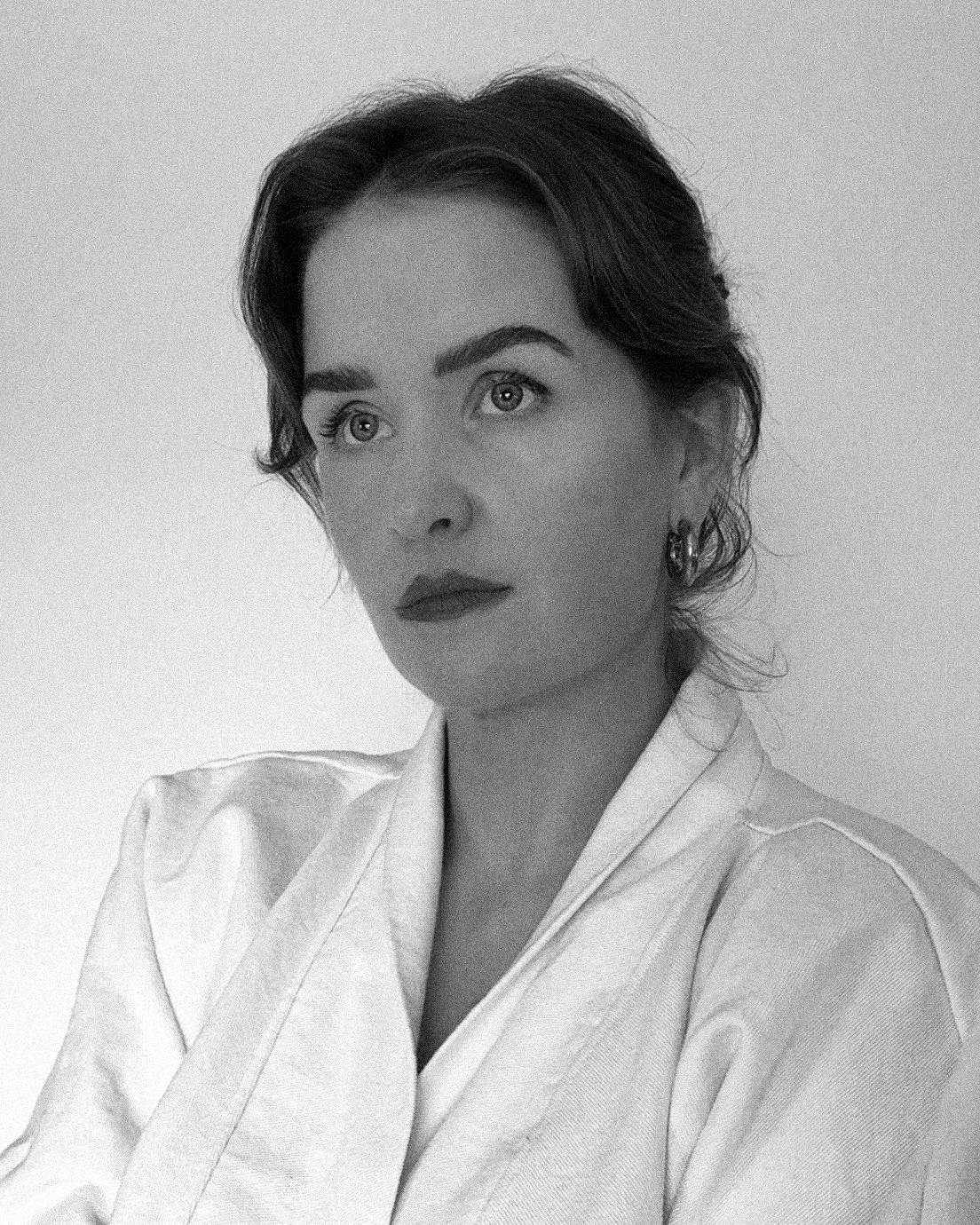 Black and white portrait of a woman with short wavy hair, wearing earrings and a light-colored blouse, looking slightly to the side.