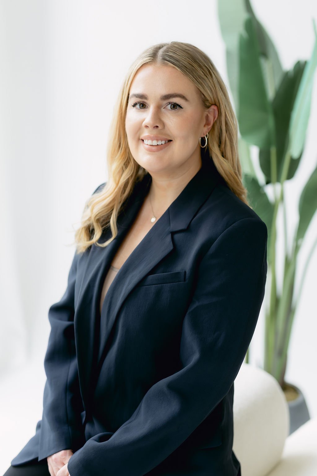 Laura Smith, Headshot.
A woman with blonde hair wearing a navy blazer, smiling, in an office with large green plants in the background.
