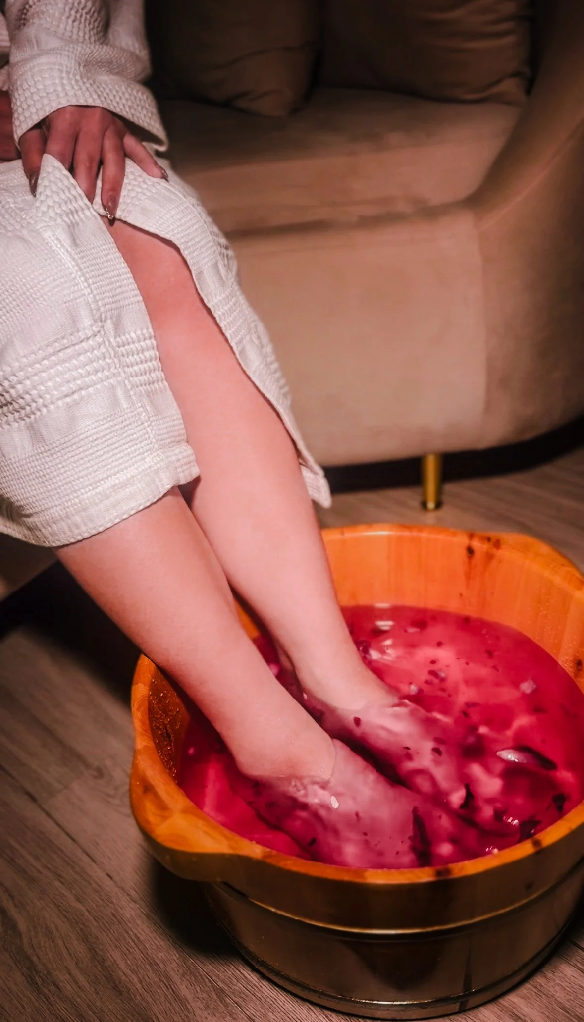lady soaking her feet in a large wooden bowl filled with pinkish-red water and fruit.