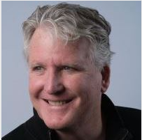 A smiling man with gray, wavy hair and wearing a black jacket.