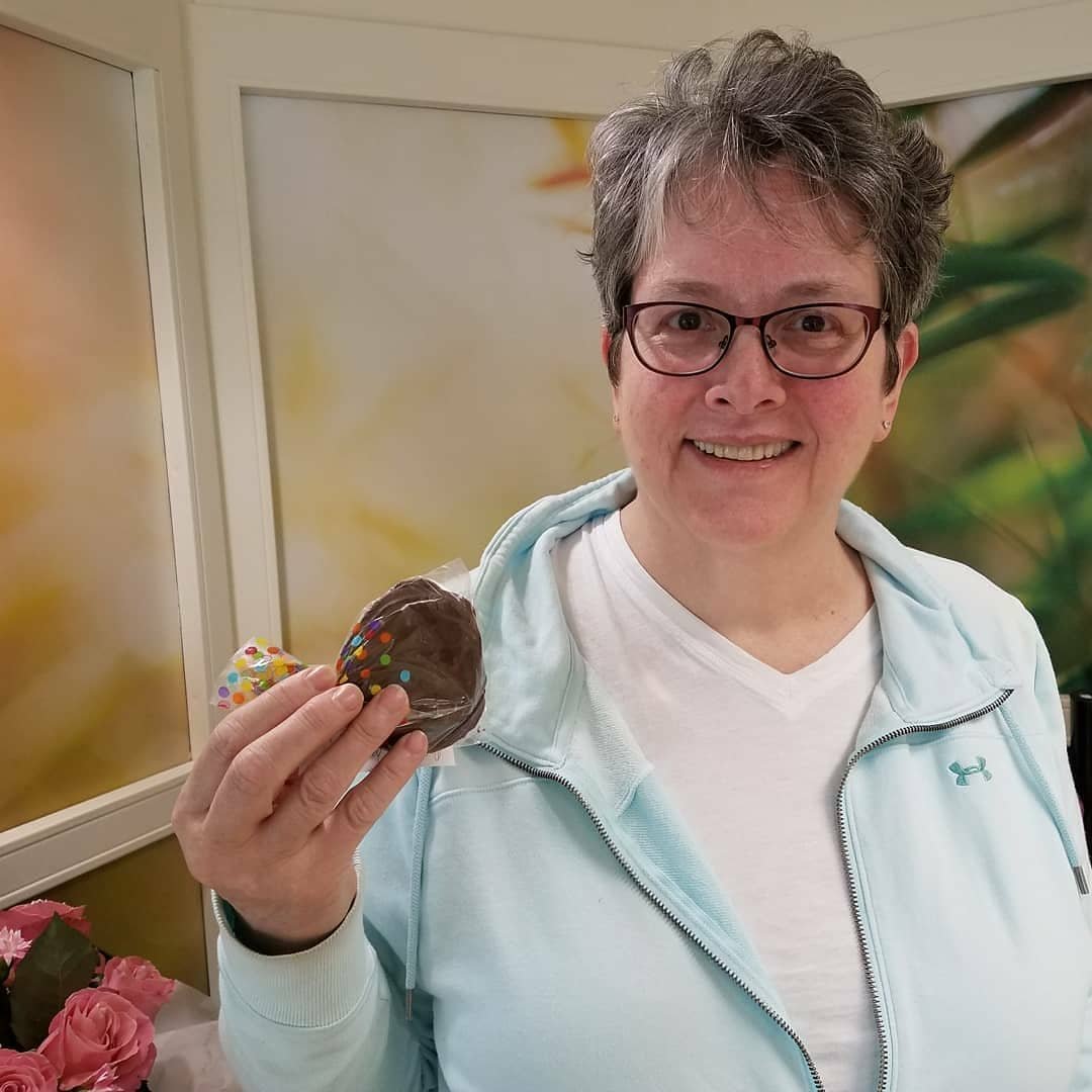 A woman with glasses and short gray hair smiling and holding a peppermint patty.