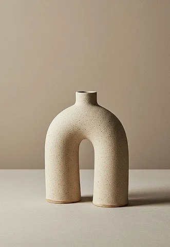 A beige, U-shaped ceramic vase on a white surface against a neutral background.