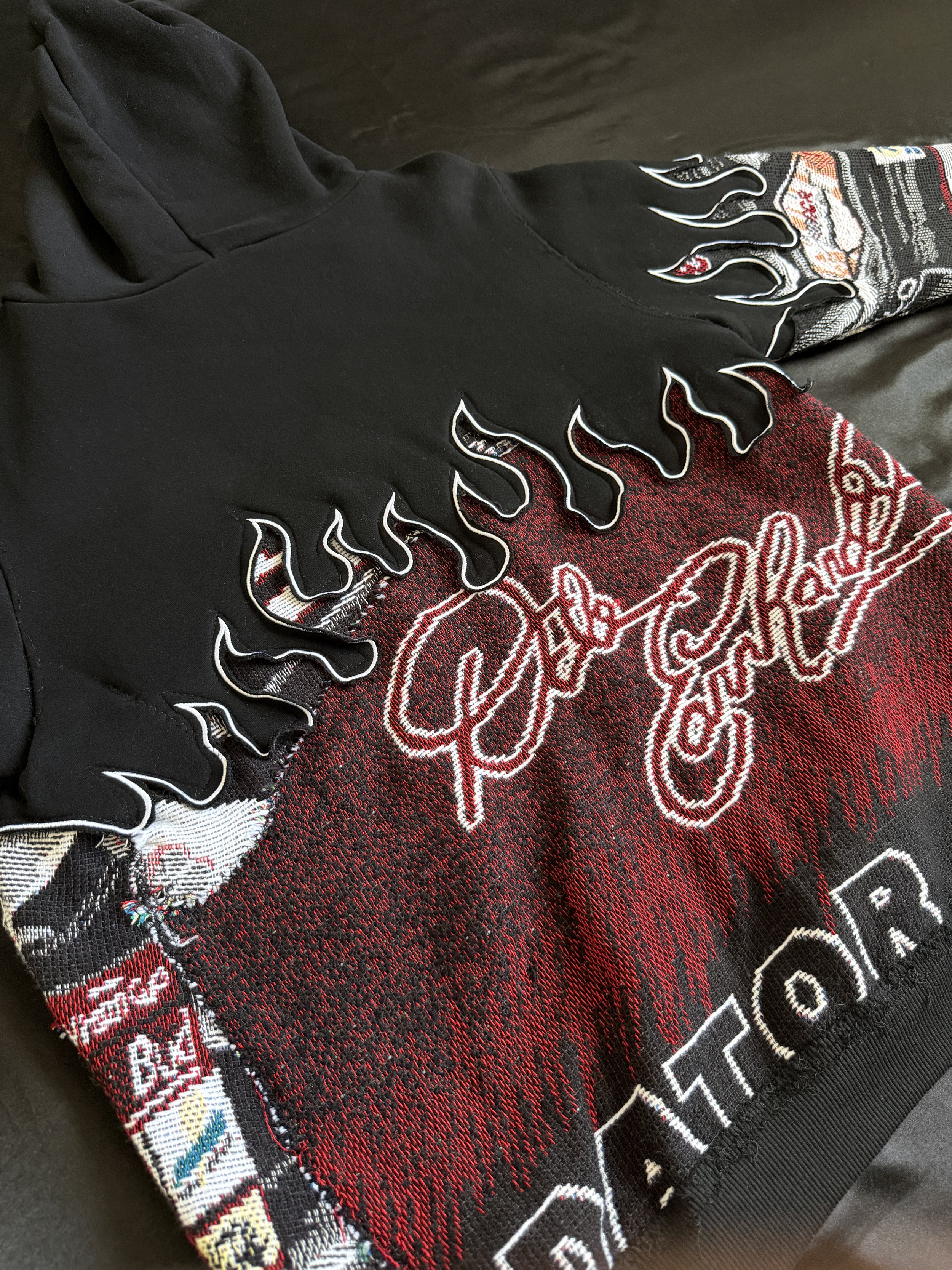 A black hoodie with fiery flame designs on the sleeves and red and white embroidered text on the front.