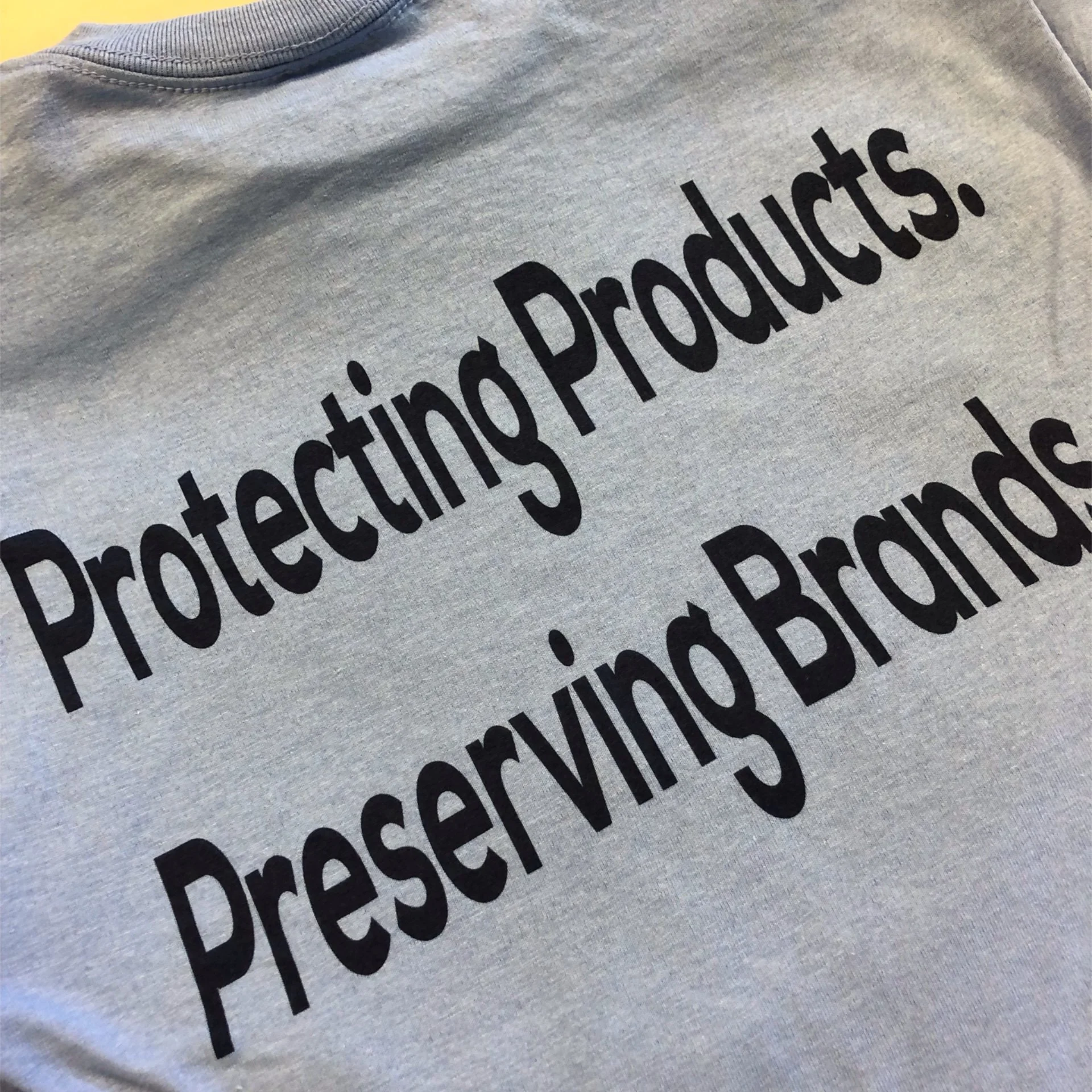 Close-up of a light gray fabric shirt with black text that reads 'Protecting Products' in large letters.