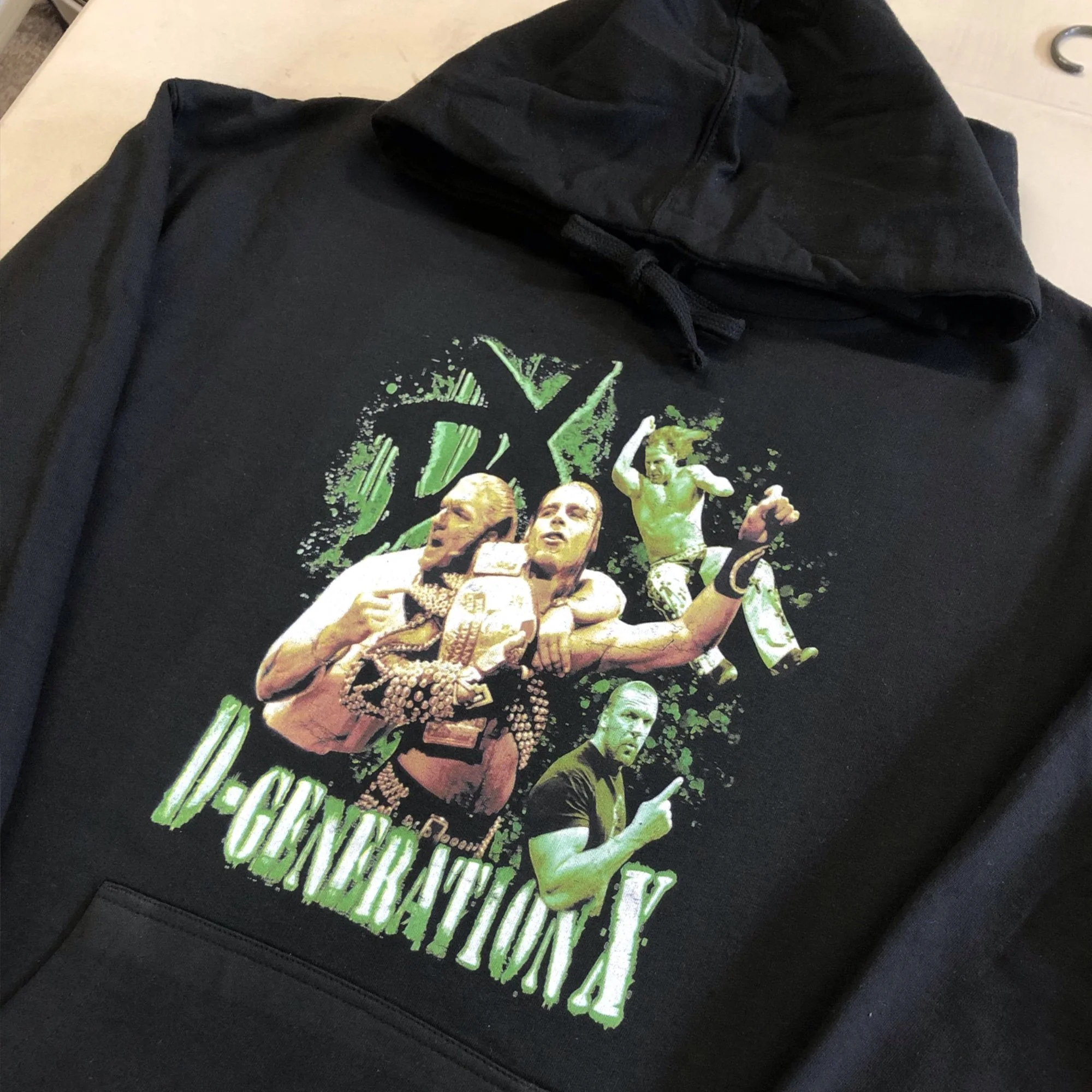 Black hoodie with a colorful graphic print of boxers fighting, including the faces of male fighters, on top of a black sweatshirt, resting on a table.