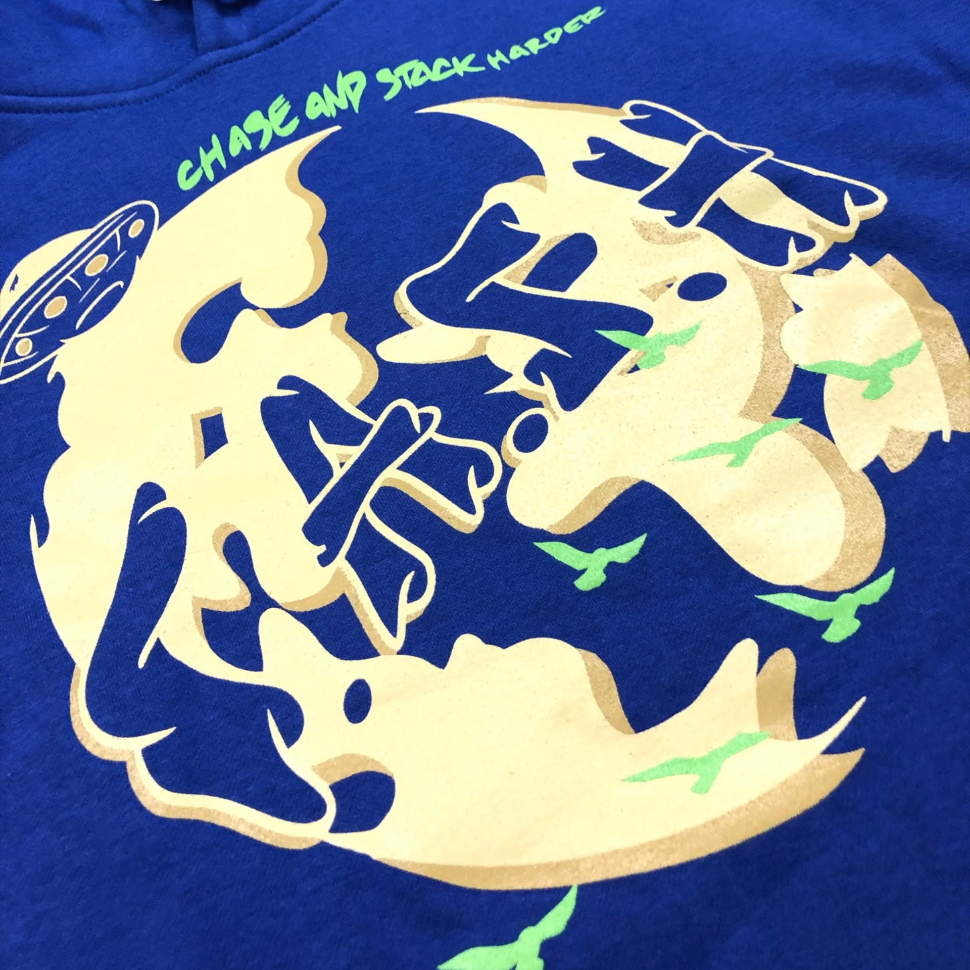 A design on a blue fabric featuring a stylized illustration of a skeleton holding an unconscious person, with green gas clouds and the words 'CHOOSE AND STACK HARDER' in lime green.