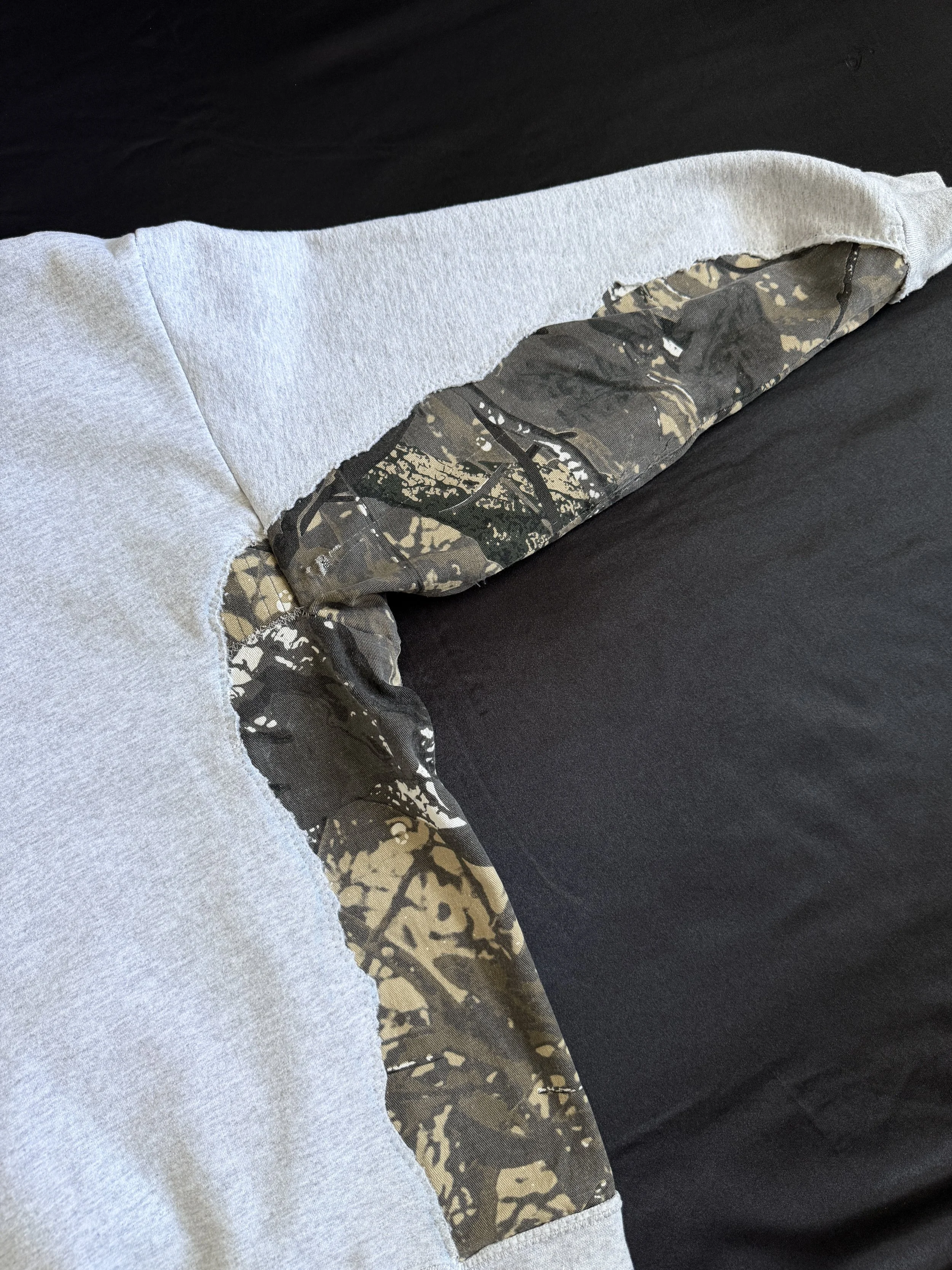 Close-up of a gray hoodie with a camouflage pattern on the sleeve, lying on a dark surface.