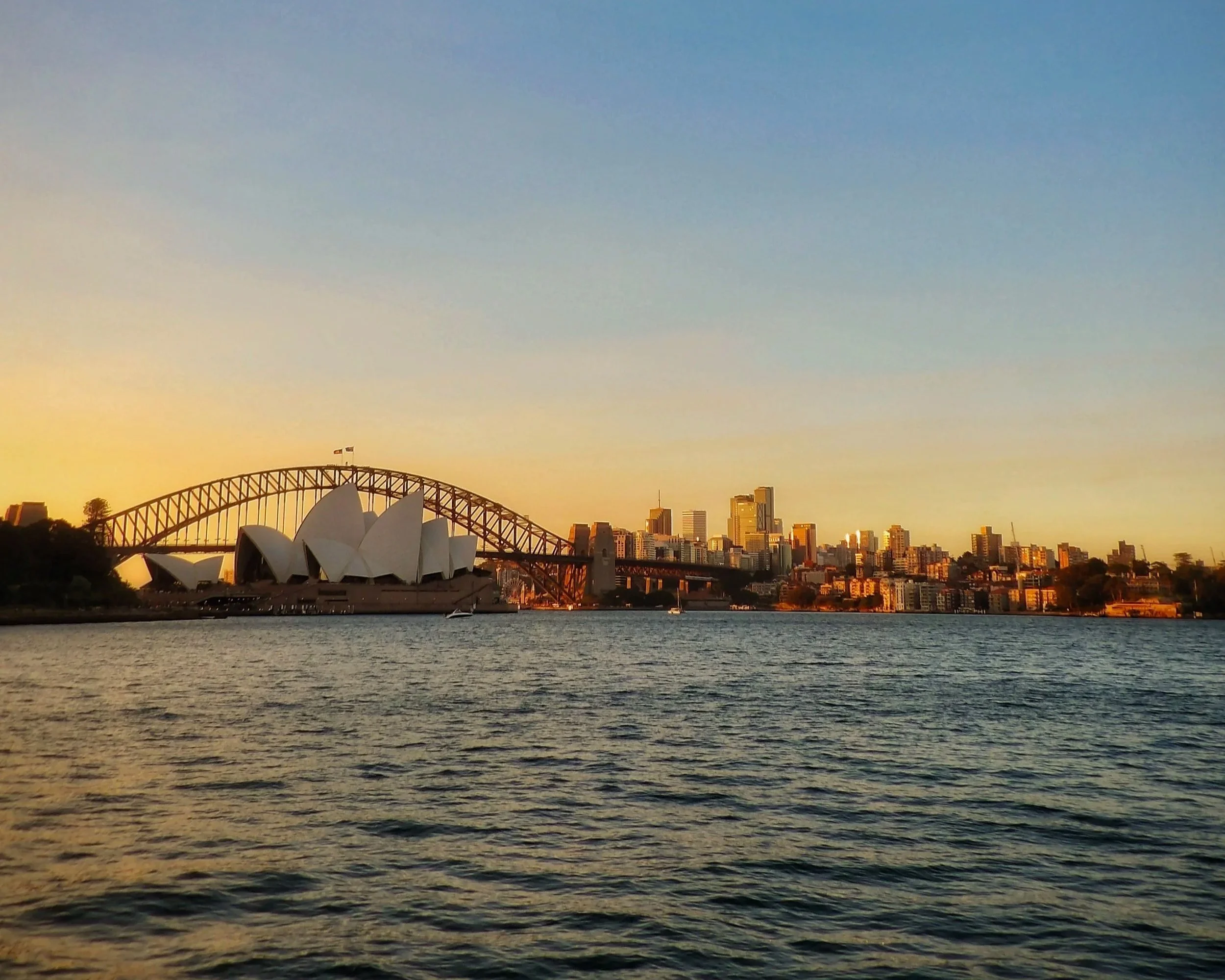 Sydney Opera House and Harbour Bridge skyline at sunset across the water.