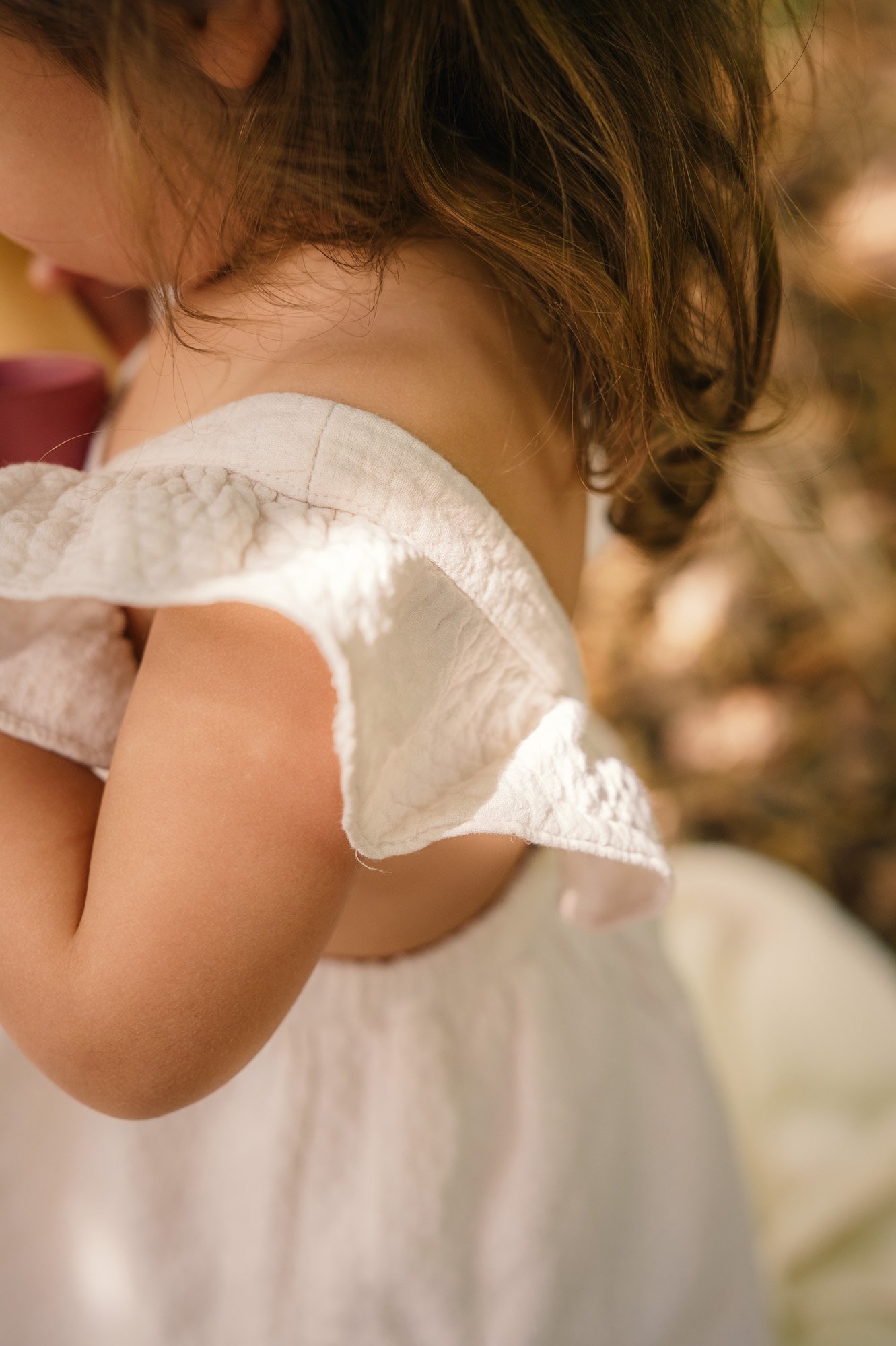 Close-up of a young child with curly hair hugging a doll dressed in a white dress.
