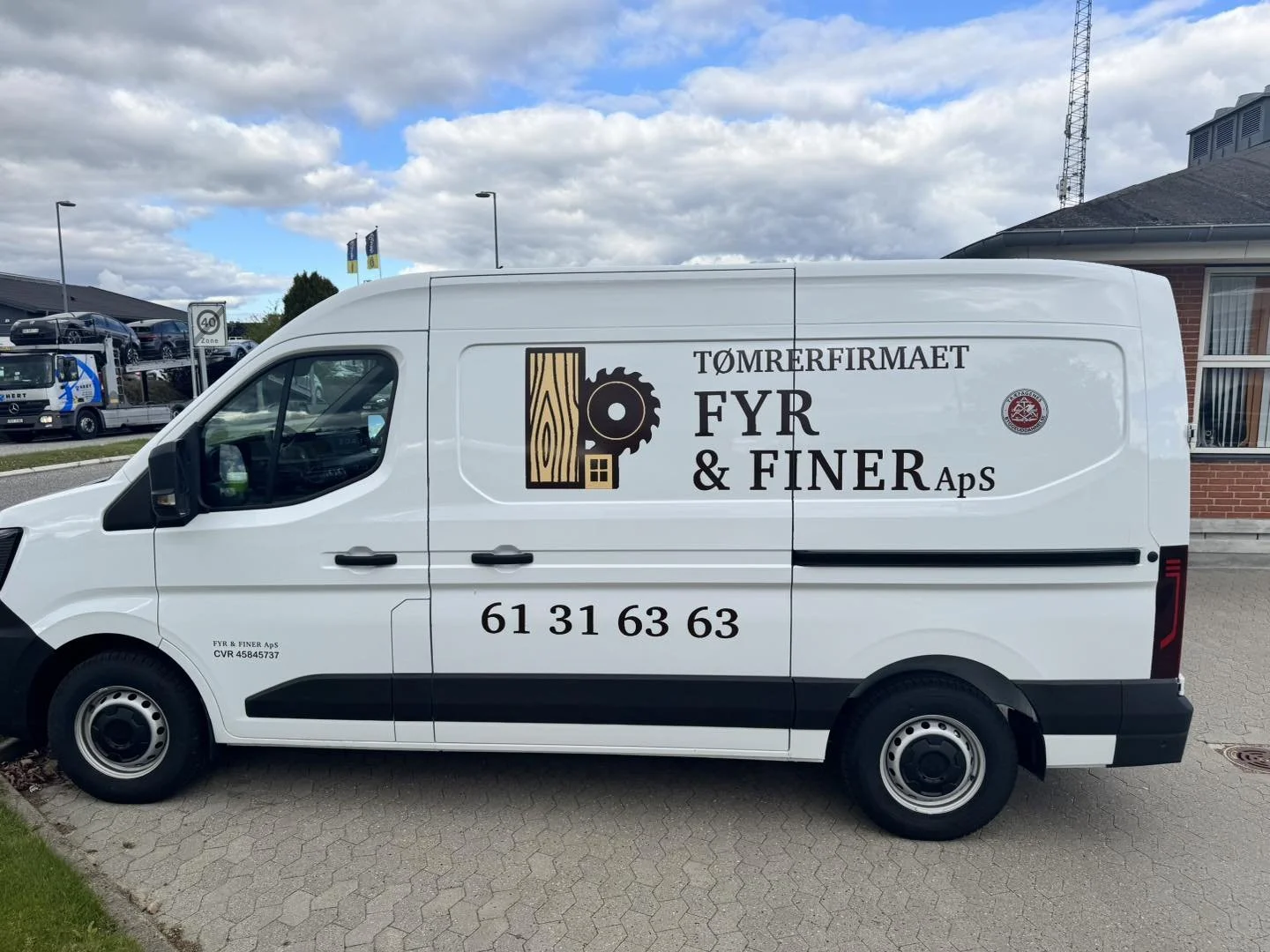 Hvid erhvervsvarebil med logo og kontaktinformation for tømrervirksomhed. Logo viser en træstamme og savklinge.