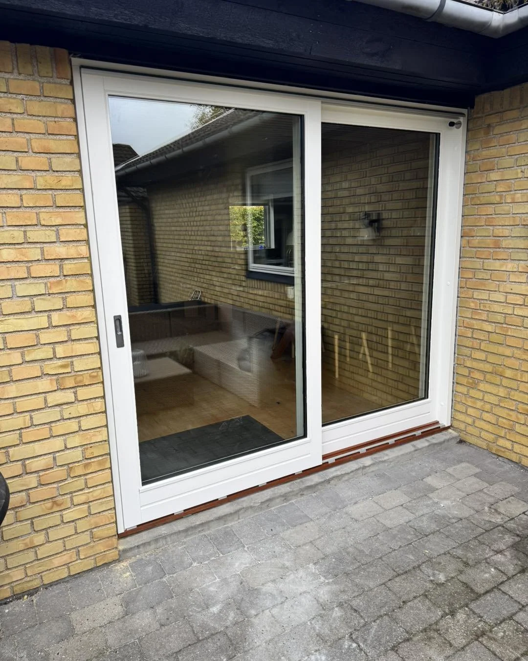 Udendørs havedør med glas, beliggende på en brostensbelægning foran et hus med gulbrun mursten.