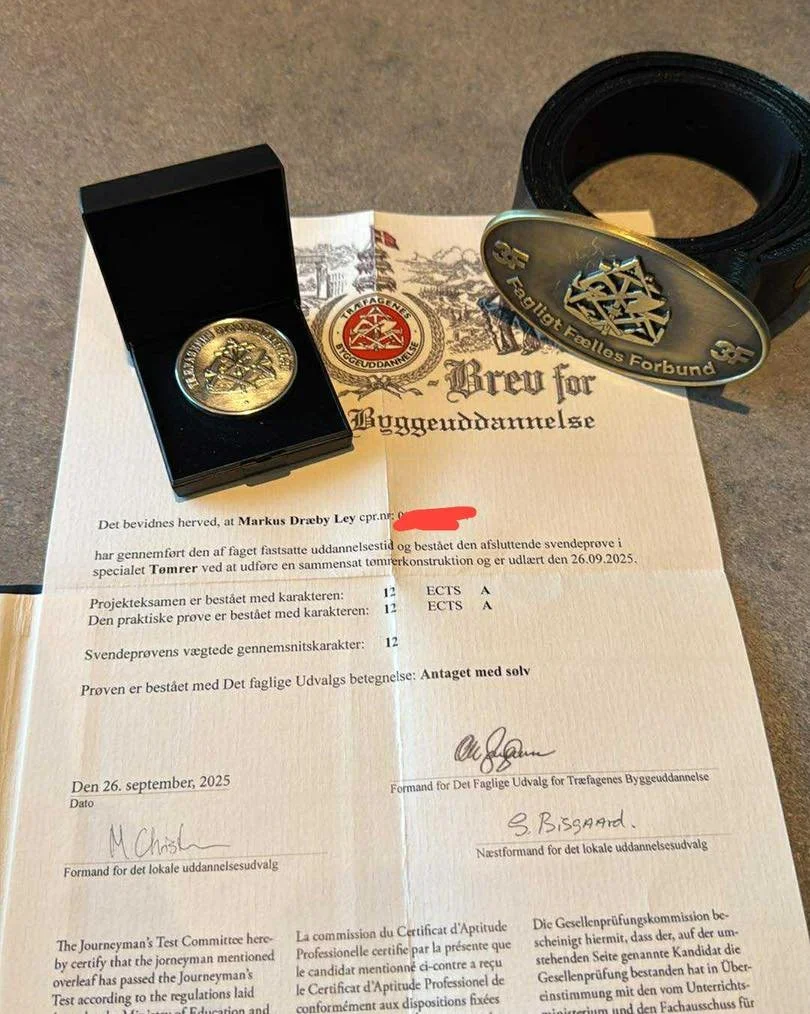 Diplom og medalje til bygguddannelse, med papirer og bælte.