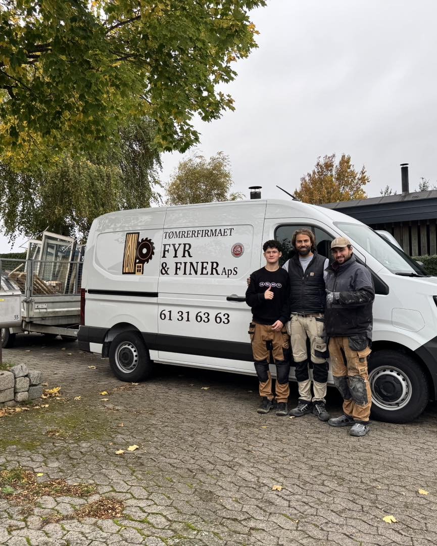 Tre personer står foran en firma-udrykning bil med teksten 'TØMRERFIRMAET FYR & FINER ApS' og telefonnummer, i en udendørs setting med træer og en bygning i baggrunden.