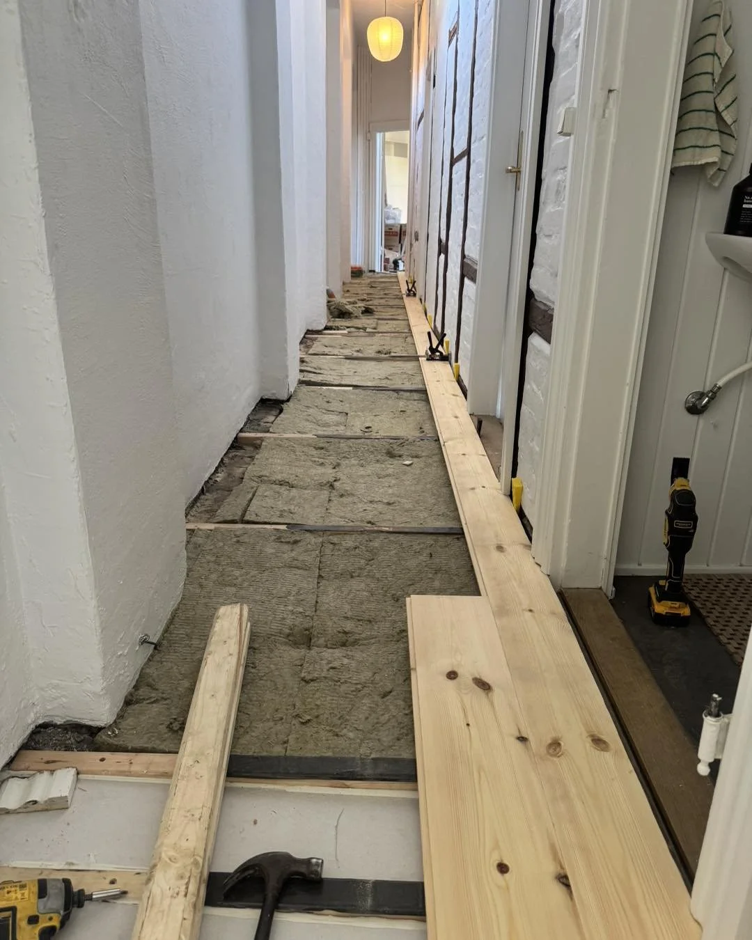 Indendørs gang under renovering med træplanker, værktøj og beklædning, hvor gulvet pudses op.