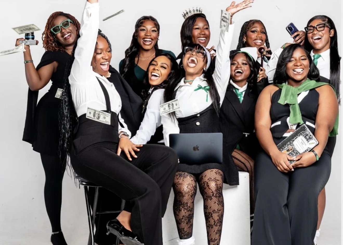 Group of women celebrating with money, laptops, and smartphones, dressed in business and casual attire, smiling and laughing against a white background.