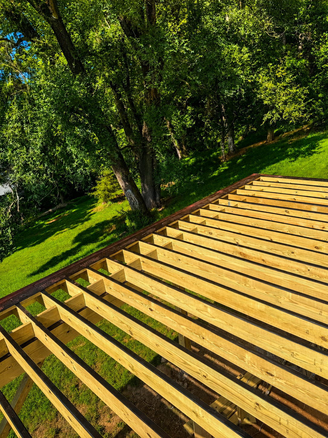 Wooden deck framework being built on a grassy lawn with trees in the background.