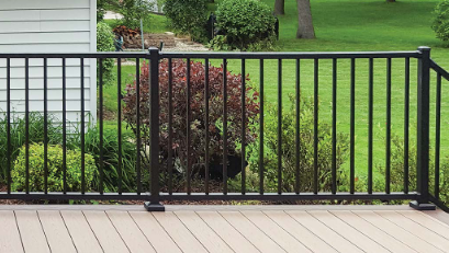 A black metal fence on a wooden deck with greenery and shrubs in the background.