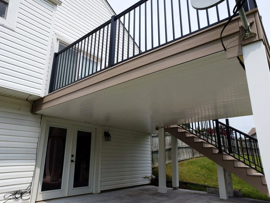 Exterior shot of a two-story house with a covered patio beneath the upper deck, which has black metal railings, and an outdoor staircase leading to the deck.
