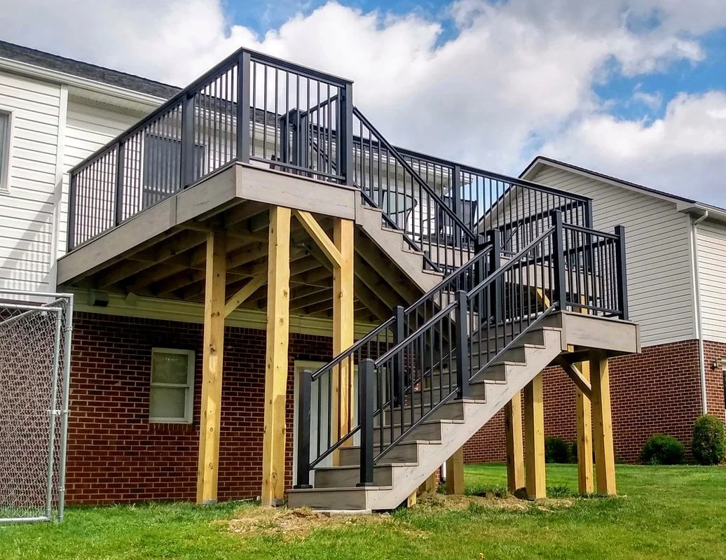 Newly constructed wooden and metal staircase leading from backyard to second-story deck of a house.