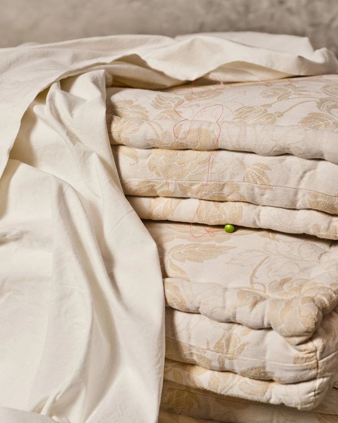 Une pile de lit avec des matelas à motifs, une couverture beige, une épingle de couture et un fil rouge.
