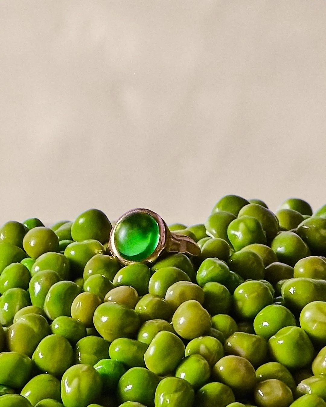 Un anneau avec une pierre verte posé sur un tas de pois verts.