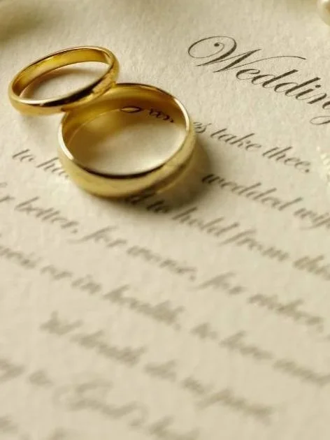 Two gold wedding rings on top of a wedding invitation.