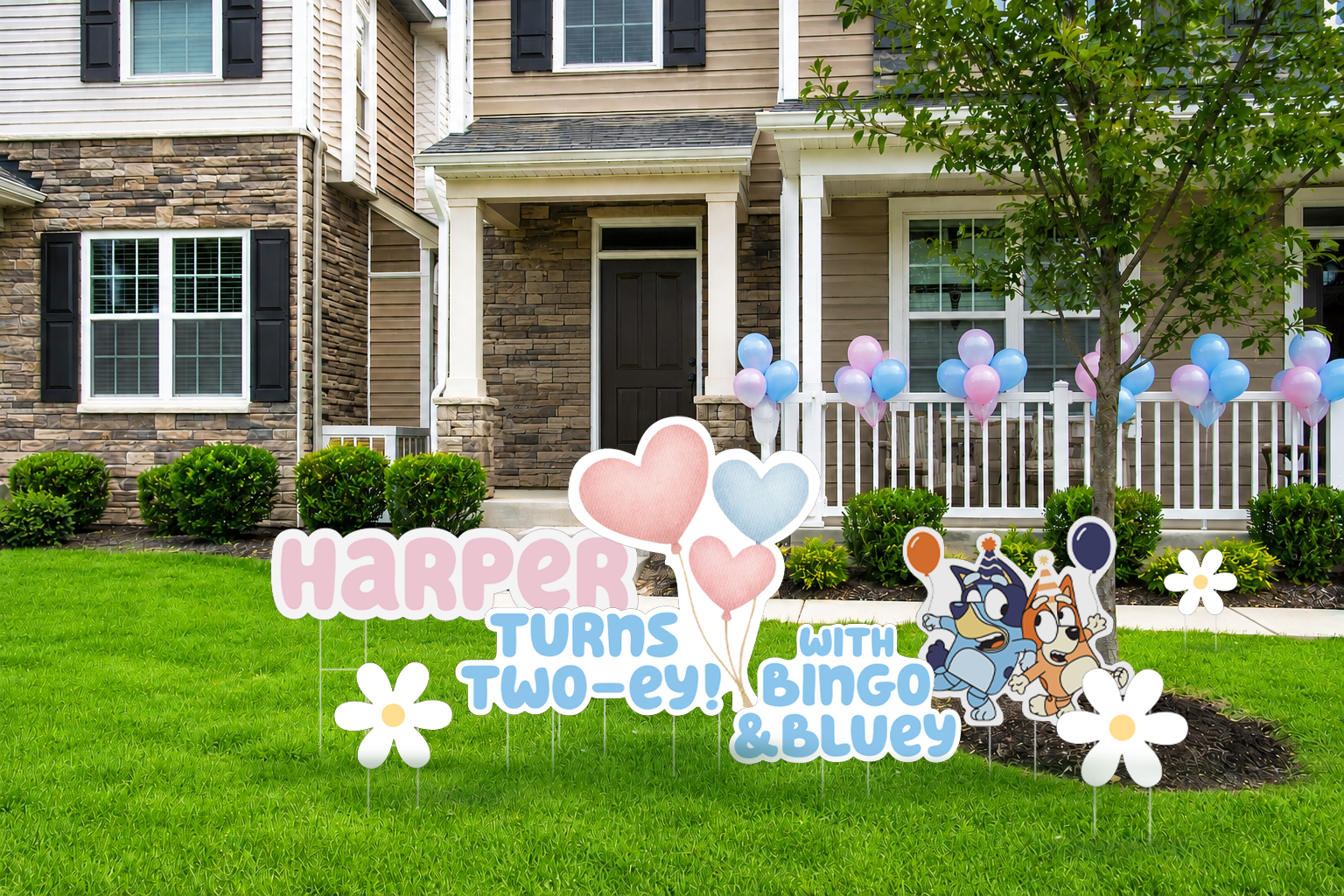 Front yard of a house decorated for a child's birthday party with balloons and signs featuring cartoon dogs. The signs say 'Harper turns two-ey! with Bingo & Bluey.' There are pink and blue balloons, white daisies, and a green lawn in front of the house.
