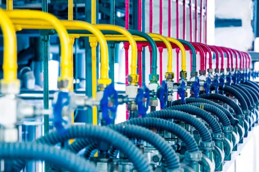 Rows of colorful pipes and hoses in a factory or industrial setting, with yellow, pink, blue, and black colors.