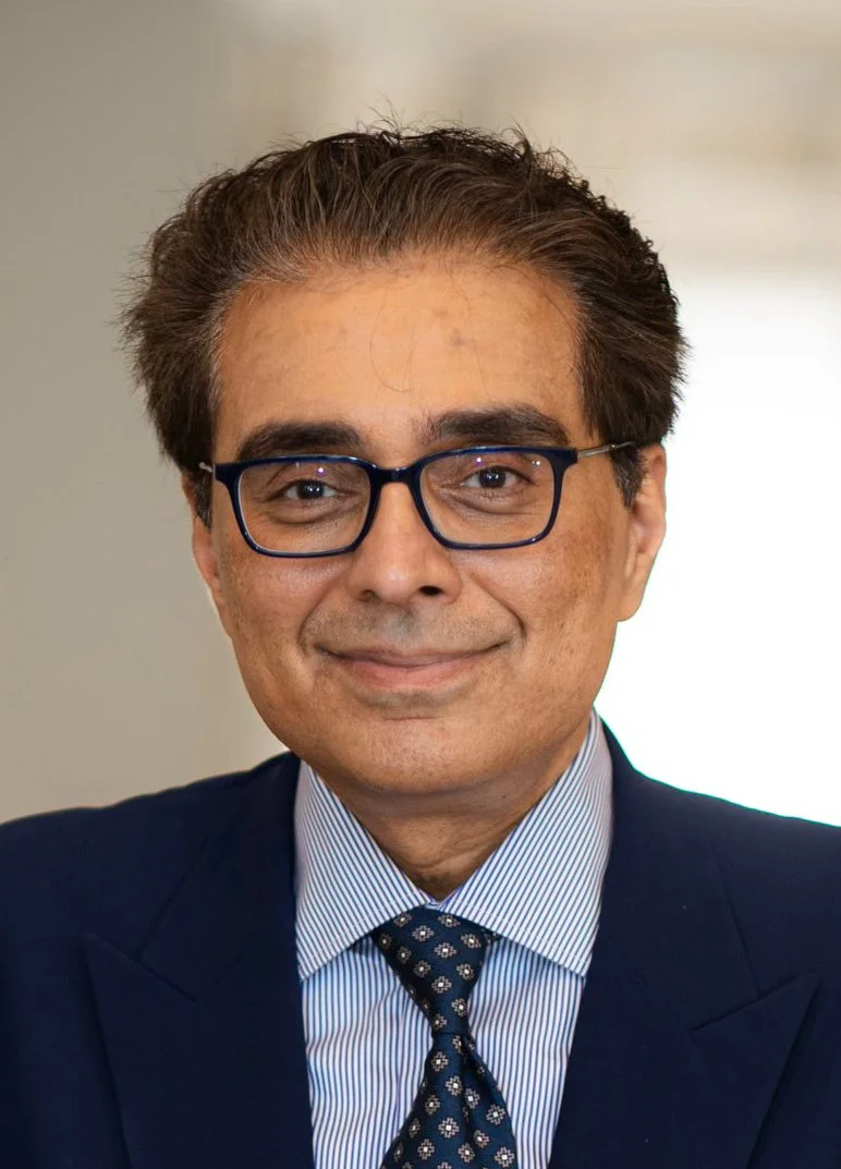 A man in a suit and tie with glasses, smiling at the camera.