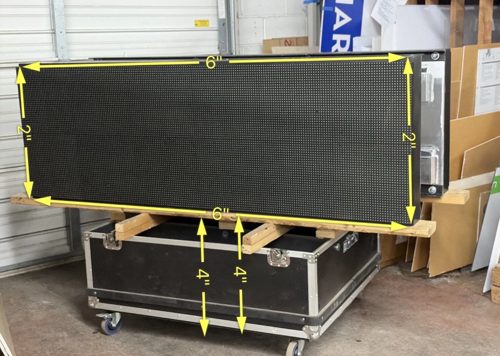 Black explosion-proof panel measuring 6 feet by 2 feet with yellow measurements marked for height and width, resting on a wooden frame on a wheeled black case in a warehouse.