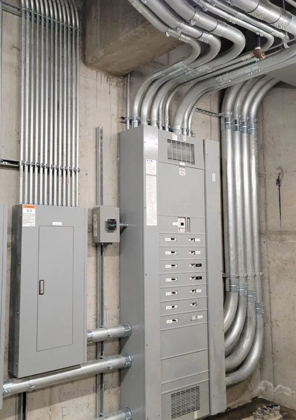 Electrical and data wiring in a concrete room with metal conduits, a gray electrical panel, and cable management.