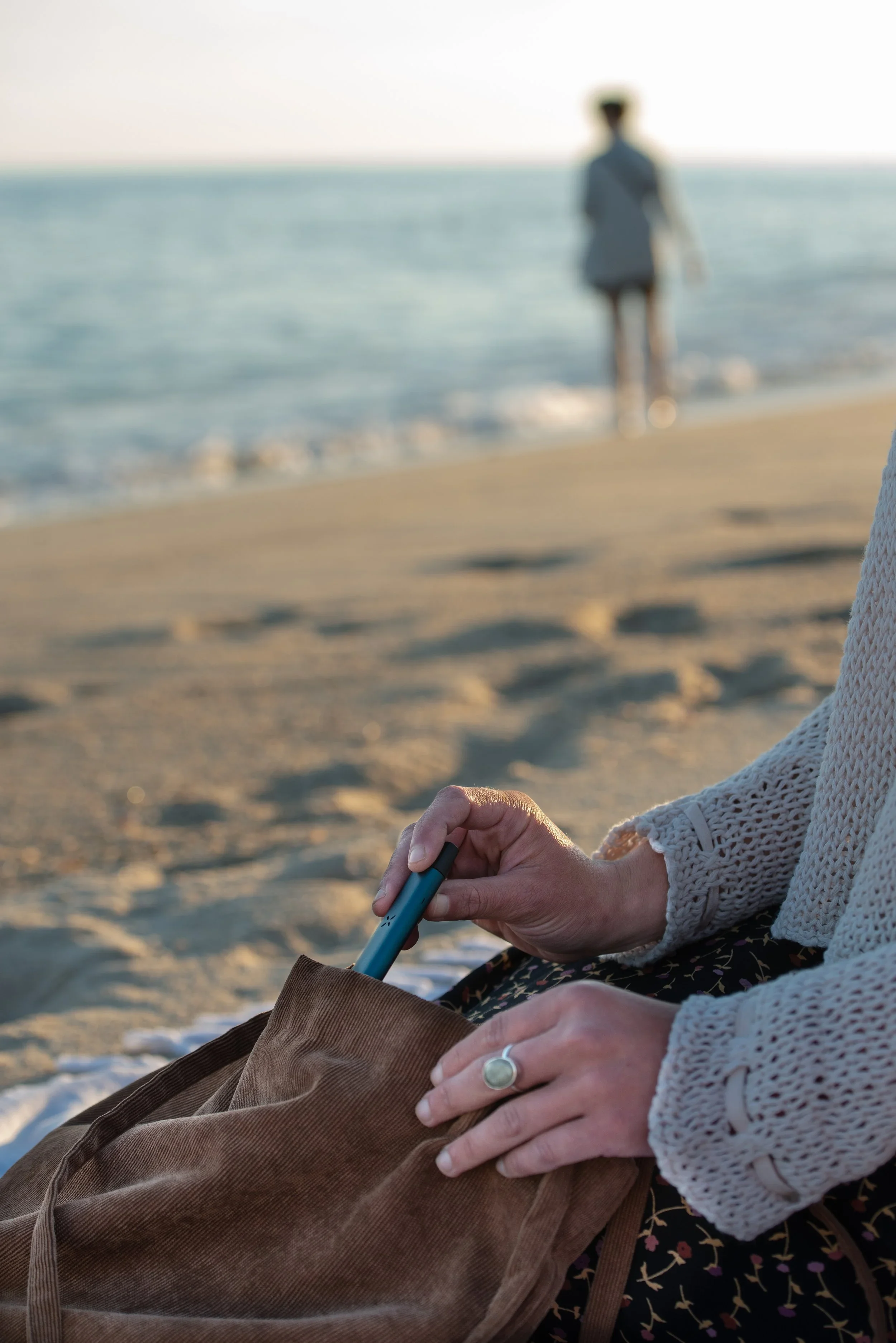 A woman's hand pulling a vaporizer out of her purse on the beach